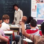 A teacher writing at a desk, representing a recommender drafting a letter of recommendation for a college applicant