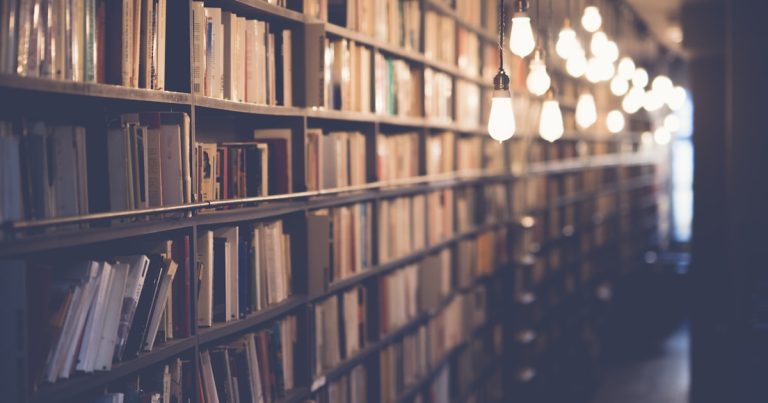 Student reading a book in a library, preparing for the enhanced ACT Reading section