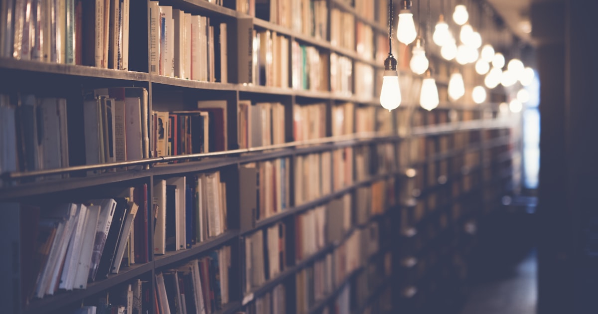 Student reading a book in a library, preparing for the enhanced ACT Reading section