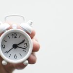 Hand holding a small alarm clock, representing extended time accommodations on the digital SAT