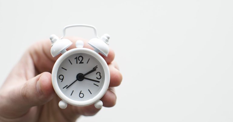 Hand holding a small alarm clock, representing extended time accommodations on the digital SAT