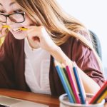High school senior drafting college supplemental essays on a laptop with a notebook of Why Us research notes