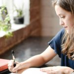 A student writing at a desk with a wristwatch on, preparing for ACT test day