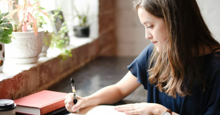 A student writing at a desk with a wristwatch on, preparing for ACT test day