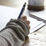 A student's notebook, pen, and laptop on a desk while planning a college application activities list ahead of the November 1 early deadline