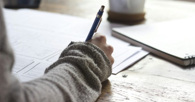 A student's notebook, pen, and laptop on a desk while planning a college application activities list ahead of the November 1 early deadline